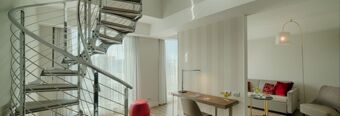 Spiral metal staircase next to a desk with chair and lamp in a bright room at NH Collection Roma Centro hotel