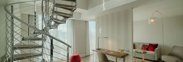 Spiral metal staircase next to a desk with chair and lamp in a bright room at NH Collection Roma Centro hotel