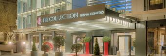 Entrance of NH Collection Roma Centro hotel with illuminated signage, glass doors, and potted plants at night