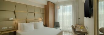 Hotel bedroom at NH Collection Roma Centro with a large bed, padded headboard, desk, chair, and large window with sheer curtains