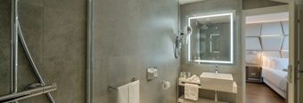 Modern bathroom with illuminated mirror, sink, towel rack, and glimpse of bedroom at NH Collection Roma Centro