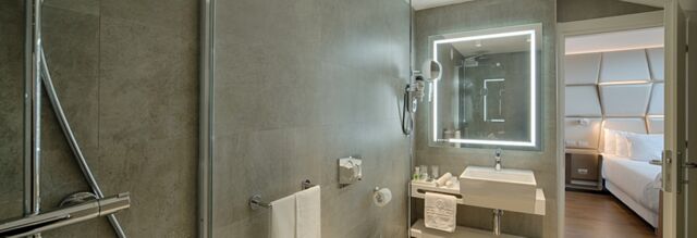 Modern bathroom with illuminated mirror, sink, towel rack, and glimpse of bedroom at NH Collection Roma Centro