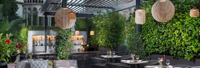 Outdoor dining area at NH Collection Roma Centro with round tables, black chairs, hanging wicker lamps, and green plants around
