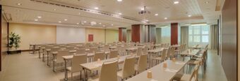 Conference room at NH Collection Roma Centro with rows of tables and chairs, paper cups, notepads, and a projector screen