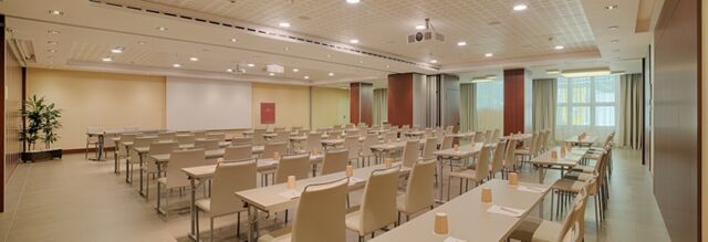 Conference room at NH Collection Roma Centro with rows of tables and chairs, paper cups, notepads, and a projector screen