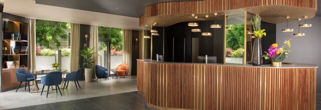 Reception area at NH Collection Roma Centro with curved wooden desk, pendant lights, seating area, and large windows showing greenery outside