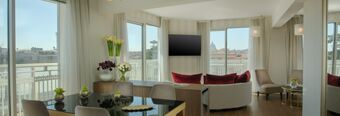 Spacious room at NH Collection Roma Centro with large windows, a dining table, chairs, flowers, and a curved sofa with red cushions
