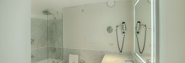Modern bathroom at NH Collection Roma Centro with marble sink, illuminated mirror, wall-mounted hairdryer, shower, and towel rack