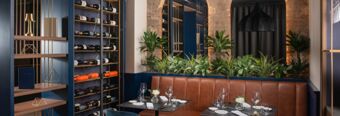 Modern dining area at NH Collection Roma Centro with leather bench seating, wine racks, green plants, and set tables