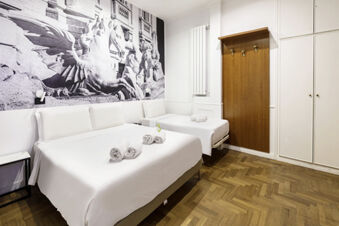 Two neatly made beds with white linens and rolled towels in a room at B&B Hotel Roma Italia Viminale with wood flooring and a black and white mural