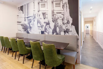 Dining area with green chairs, wooden tables, gray bench seating, and a black and white mural at B&B Hotel Roma Italia Viminale