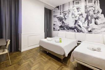 Hotel room at B&B Hotel Roma Italia Viminale with two beds, wooden floor, gray curtains, and a large mural of statues on the wall