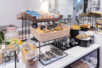 Buffet table with various pastries, cereals, cutlery, and a glass container with lemon water at B&B Hotel Roma Italia Viminale
