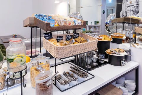 Buffet table with various pastries, cereals, cutlery, and a glass container with lemon water at B&B Hotel Roma Italia Viminale
