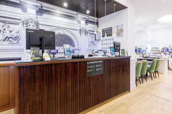Reception desk with wooden paneling, computer monitors, green chairs, and a large black and white mural at B&B Hotel Roma Italia Viminale