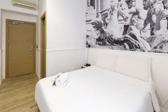Minimalist hotel room at B&B Hotel Roma Italia Viminale with white bedding, folded towels, wooden door, and black and white wall art