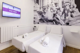 Two single beds with white linens and towels face a wall-mounted TV in a room at B&B Hotel Roma Italia Viminale