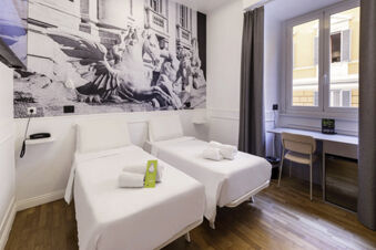 A clean hotel room with two white single beds, rolled towels, a desk with a chair, window, and large black and white mural at B&B Hotel Roma Italia Viminale