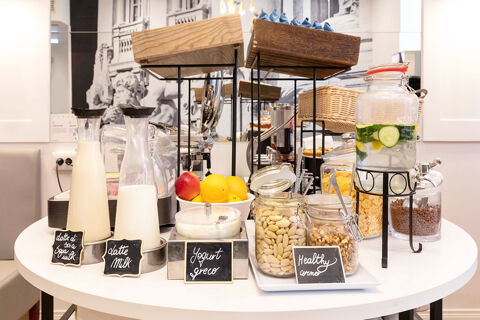 two glass bottles with soy milk and milk next to a bowl of fruit and jars of nuts and yogurt on a table at B&B Hotel Roma Italia Viminale