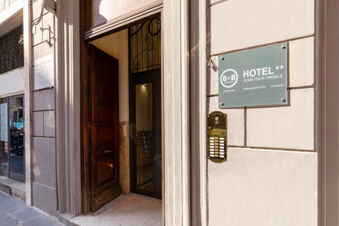 Entrance with a wooden door open leading inside a building with a sign for B&B Hotel Roma Italia Viminale visible on the wall