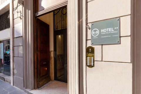 Entrance with a wooden door open leading inside a building with a sign for B&B Hotel Roma Italia Viminale visible on the wall