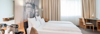 Spacious and bright hotel room at NH Hotel M&uuml;nchen Neue Messe featuring twin beds, a large window with curtains, and a work desk