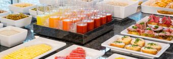 Assorted fresh juices in glasses and a variety of sliced fruits, breads, and cold cuts buffet at NH Hotel M&uuml;nchen Neue Messe