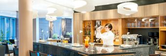 Bartender preparing a cocktail behind a dark marble bar with bottles and glasses at NH Hotel M&uuml;nchen Neue Messe