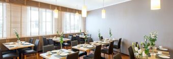 Dining area at NH Hotel M&uuml;nchen Neue Messe with multiple tables set with plates cups and floral centerpieces under hanging lights