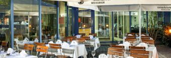 Outdoor dining area with wooden chairs and white tablecloths under large umbrellas at NH Hotel M&uuml;nchen Neue Messe