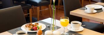 A breakfast table at NH Hotel M&uuml;nchen Neue Messe with coffee cups, orange juice, croissants, berries, boiled egg, and a flower vase