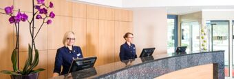 Two female receptionists standing behind a granite counter with computers in the lobby of NH Hotel M&uuml;nchen Neue Messe
