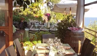 Terrazza ristorante con tavoli coperti, vista mare e tanto verde alla Pensione Ristorante Bellavista, invitante e soleggiata.