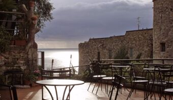 Outdoor patio area with metal tables and chairs overlooking the sea and stone walls at Pensione Ristorante Bellavista