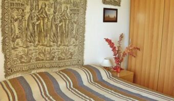 A bedroom in Pensione Ristorante Bellavista with a striped bedspread, a wall tapestry, nightstand, lamp, dried flowers, and wooden wardrobe
