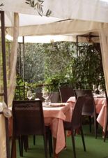 Accogliente spazio esterno della Pensione Ristorante Bellavista con tavoli apparecchiati, tovaglie rosa tenue e uno sfondo verde di foglie.