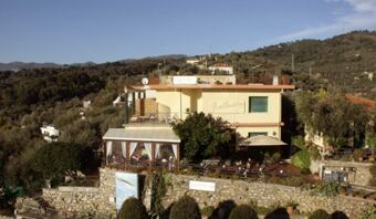 Yellow two-story Pensione Ristorante Bellavista building with outdoor seating surrounded by trees and hills in the background
