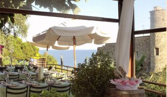 Vista della soleggiata terrazza esterna con tavoli coperti, ombrellone e vista sul mare e sugli edifici storici della Pensione Ristorante Bellavista.