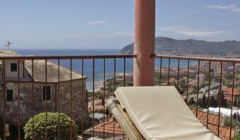 View from a balcony at Pensione Ristorante Bellavista showing a railing, a lounge chair, rooftops, ocean, and distant hills in clear weather