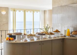 Breakfast buffet with croissants, muffins, cakes, bread rolls, fruits, and orange juice in B&B Hotel Diano Marina Palace dining area
