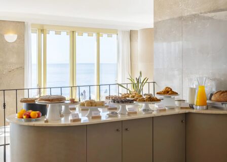 Breakfast buffet with croissants, muffins, cakes, bread rolls, fruits, and orange juice in B&B Hotel Diano Marina Palace dining area