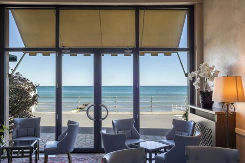 Glass doors with yellow awnings open to a sea view with seating and a lamp inside at B&B Hotel Diano Marina Palace