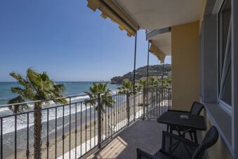 Balcony with table, chairs, and awnings overlooking palm trees, beach, blue sea, and distant hillside at B&B Hotel Diano Marina Palace