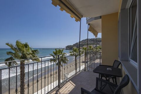 Balcony with table, chairs, and awnings overlooking palm trees, beach, blue sea, and distant hillside at B&B Hotel Diano Marina Palace