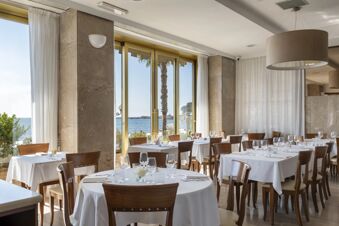 Dining area at B&B Hotel Diano Marina Palace with round and square tables covered in white cloths and ocean view windows
