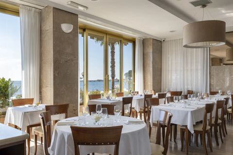 Dining area at B&B Hotel Diano Marina Palace with round and square tables covered in white cloths and ocean view windows