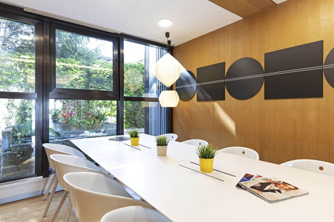 Bright meeting room at B&B Hotel Udine with a long white table, white chairs, plants, magazines, and large glass windows