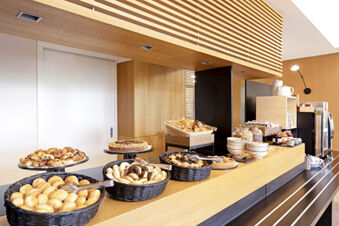 Breakfast buffet with assorted pastries, cookies, croissants, cereals, and bowls on a counter at B&B Hotel Udine