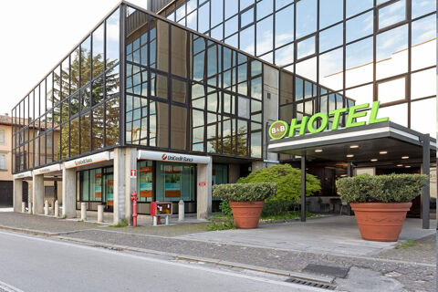 B&B Hotel Udine entrance with large green sign on a modern glass building next to UniCredit Banca location and plants