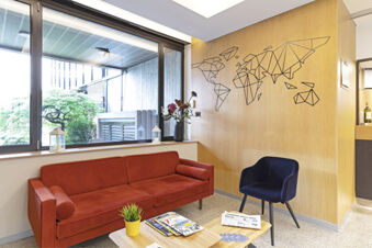 Modern lobby area at B&B Hotel Udine with a red sofa, blue chair, wooden coffee table, and geometric world map wall art